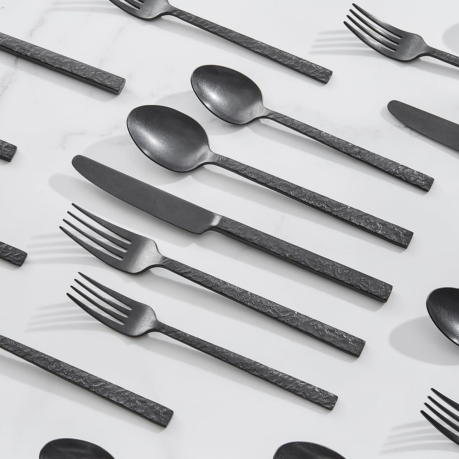 Black hammered stainless steel silverware set with fork, knife, and spoon pieces arranged on white background — view 2