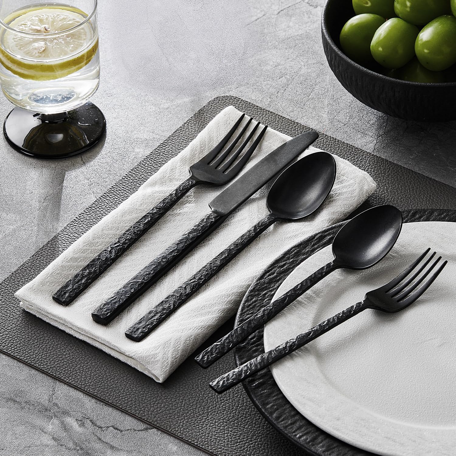 Black hammered stainless steel silverware set with fork, knife, and spoon pieces arranged on white background — view 4